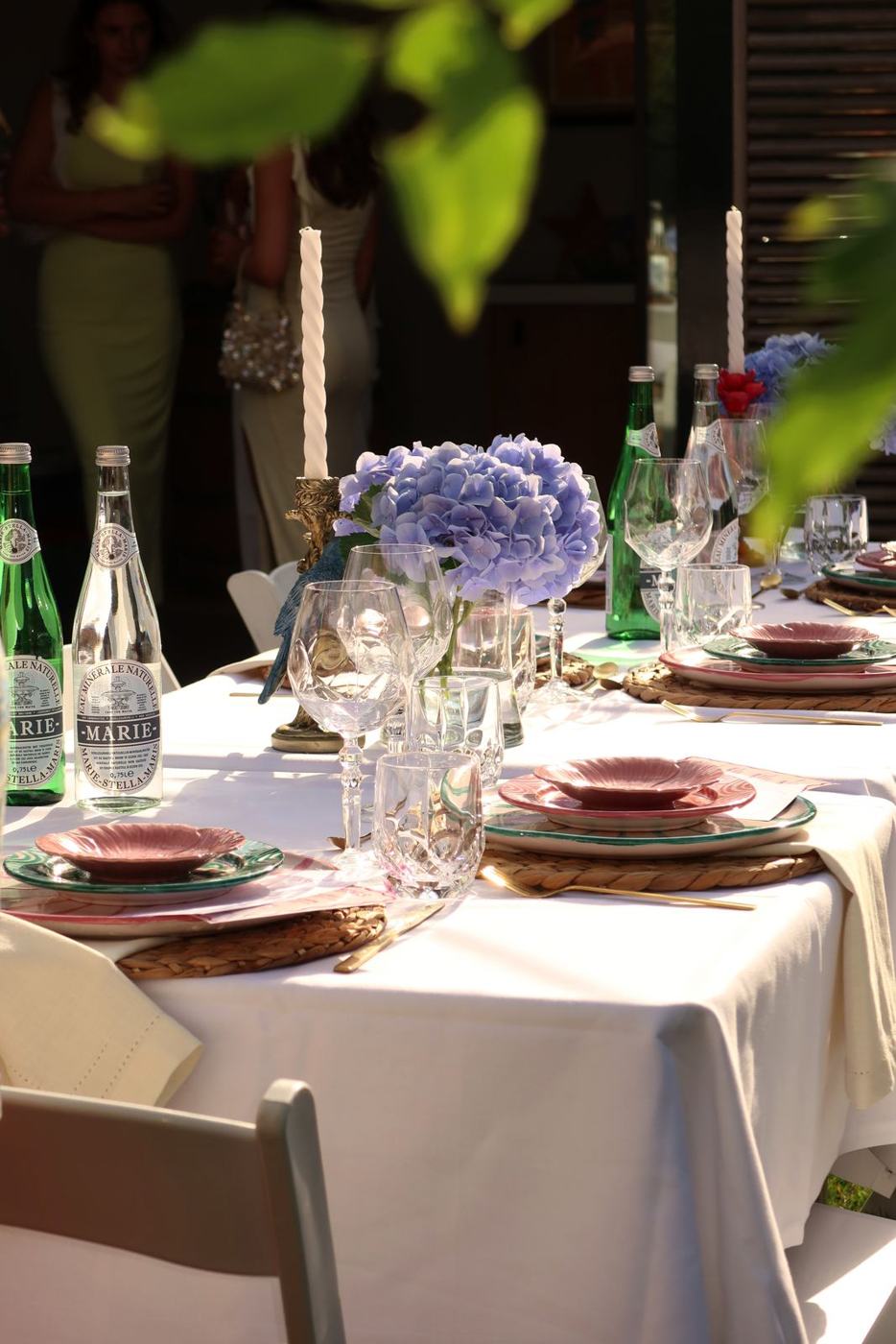 Gedekte tafel in een zomerse tuin met blauwe hortensia's en roze borden tijdens een 21-diner